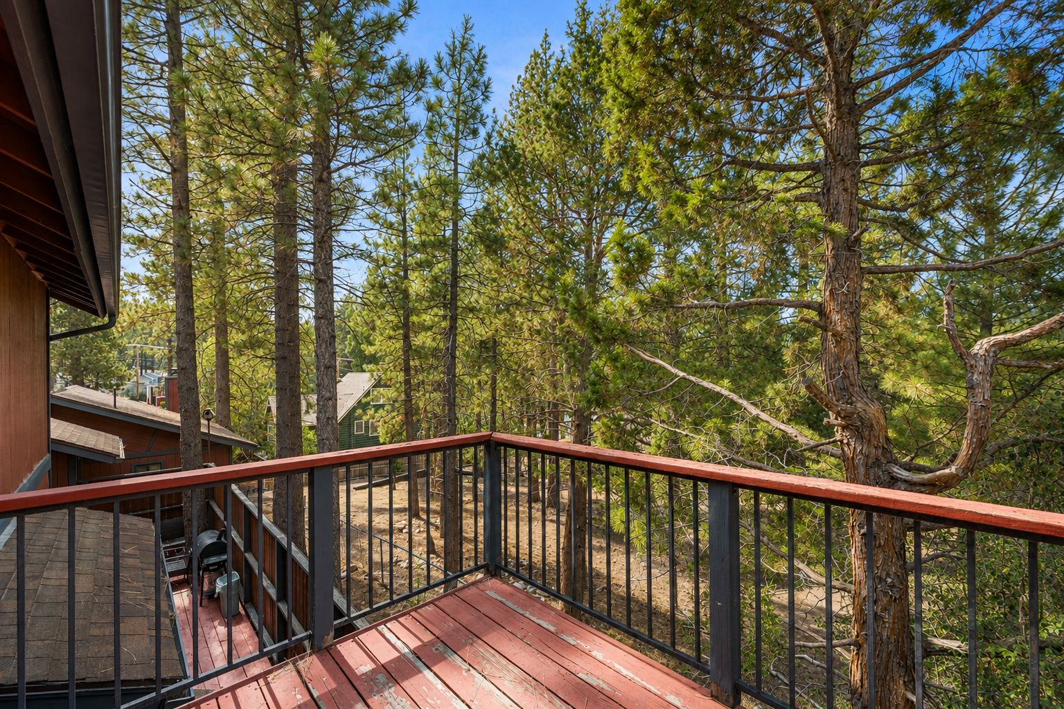 Une terrasse en bois avec une rambarde en métal, donnant sur une zone boisée.