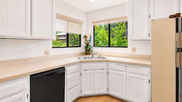 A kitchen with white cabinets, a black dishwasher, a beige refrigerator, and a window with a view of greenery.
