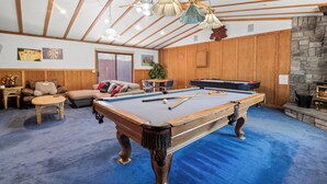 A spacious indoor area with a pool table, wooden furniture, and a stone fireplace. - Silver Rays (Big Bear Lake)