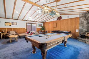 A spacious indoor area with a pool table, wooden furniture, and a stone fireplace. - Silver Rays (Big Bear Lake)