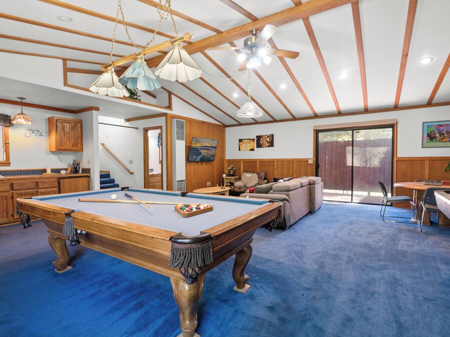 A pool table in a room with wooden beams and a blue carpet. There is a sofa and a dining table with chairs.