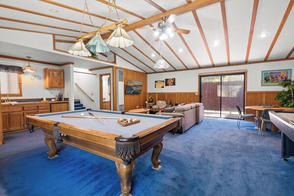 A pool table in a room with wooden beams and a blue carpet. There is a sofa and a dining table with chairs. - Silver Rays (Big Bear Lake)