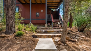 A wooden cabin with a stone staircase leading to a wooden deck, surrounded by trees and rocks. - Silver Rays (Big Bear Lake)