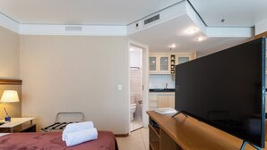 Camera d'albergo con un letto, una scrivania con televisore a schermo piatto, una lampada e vista sull'area cucina.