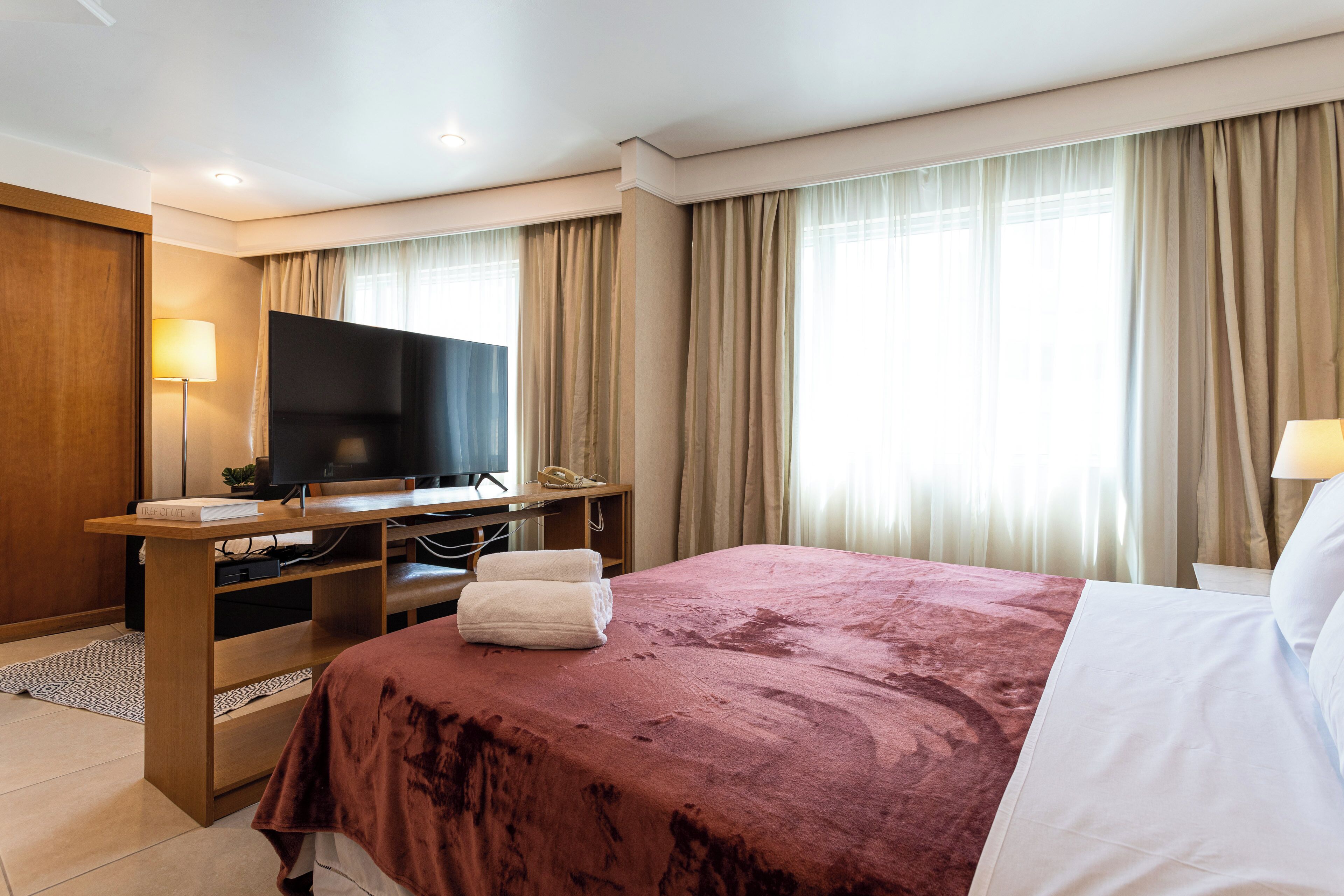 Ett hotellrum med en stor säng, ett skrivbord med en platt-TV, en telefon och ett fönster med gardiner.