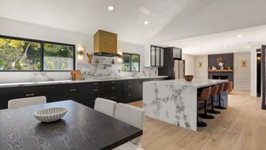 Une cuisine moderne dotée d’un îlot en marbre, de meubles noirs et d’un coin repas avec une table et des chaises en bois.