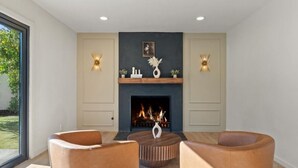 Un salon moderne avec une cheminée, deux fauteuils en cuir, une table basse ronde et des appliques murales décoratives.