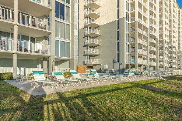 Un hotel de varios pisos con balcones, una piscina con tumbonas y una zona ajardinada.