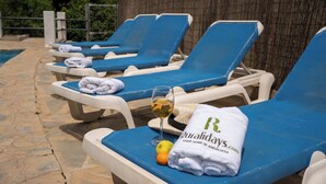 A row of blue lounge chairs with white cushions, a glass of white wine, and a towel with branding. - El Molinillo de Jimera Jimera de Libar by Ruralidays (Málaga)