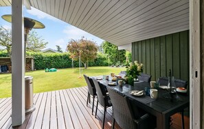 Eine Terrasse im Freien mit Holzdeck, einem Essplatz und Blick auf einen gepflegten Garten.