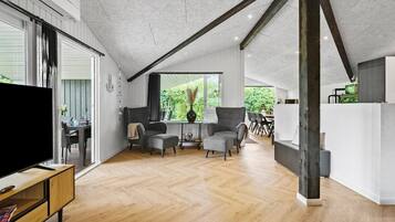 Un vaste espace de vie doté d’un plancher en bois, d’un téléviseur et d’un coin repas avec des chaises et une table.