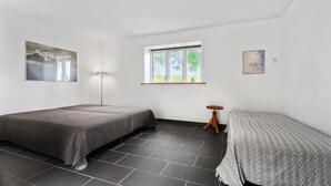 Una habitación con dos camas, una lámpara de pie, una ventana con vista a la vegetación y un cuadro en la pared.