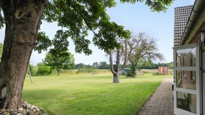Un espacio al aire libre con césped, árboles, una mesa de picnic y un edificio con techo de tejas.