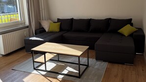Una sala de estar moderna con un sofá seccional negro, una mesa de centro de madera y un ventanal con cortinas.