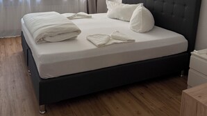 Una cama bien hecha con sábanas y almohadas blancas, un cabecero oscuro y una lámpara colgante.