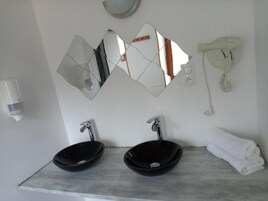 Casa de banho com duas pias pretas, um espelho, um secador de cabelo e um porta-toalhas.