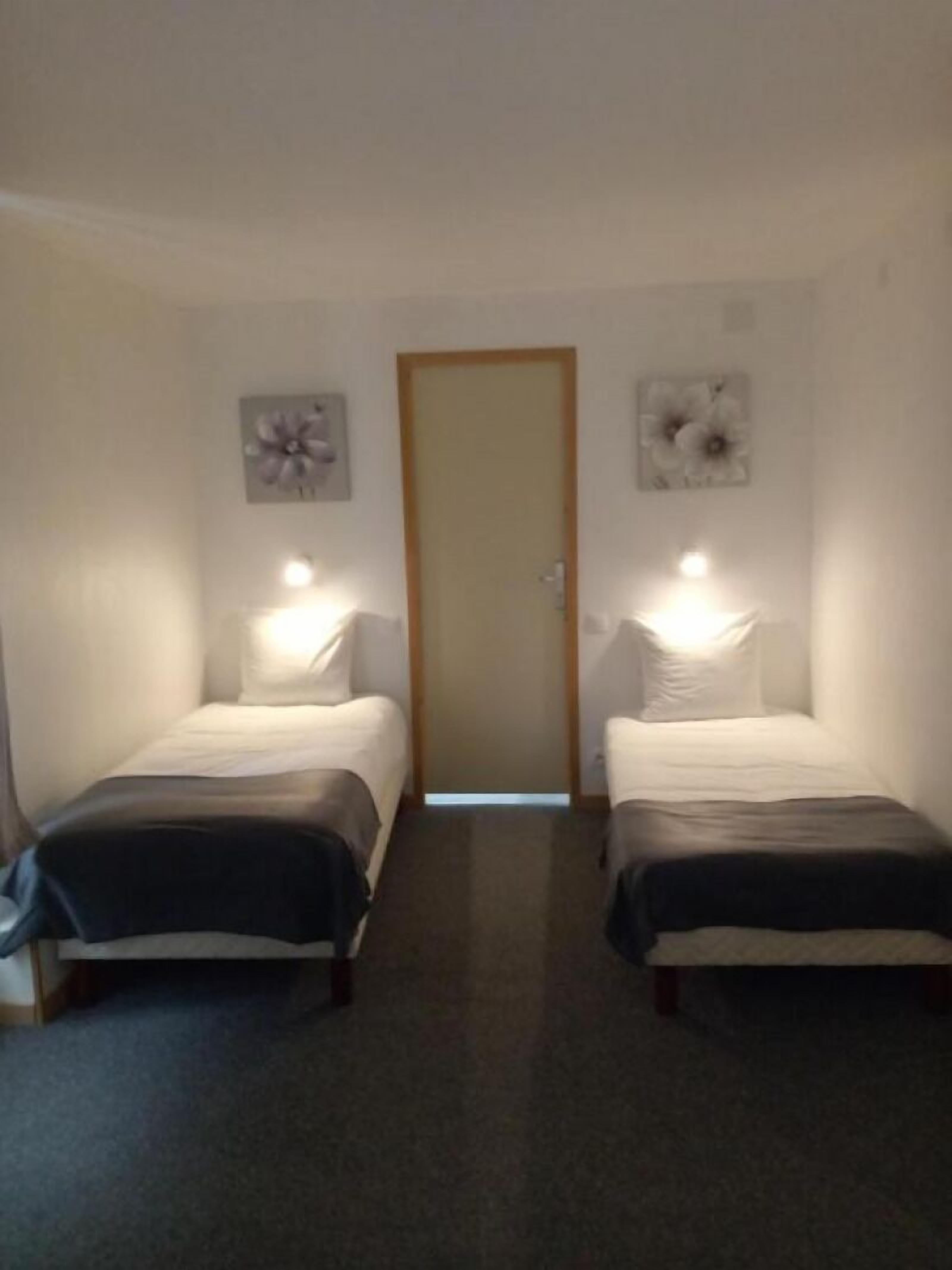 Habitación con dos camas, una puerta y luminarias fijadas a la pared.
