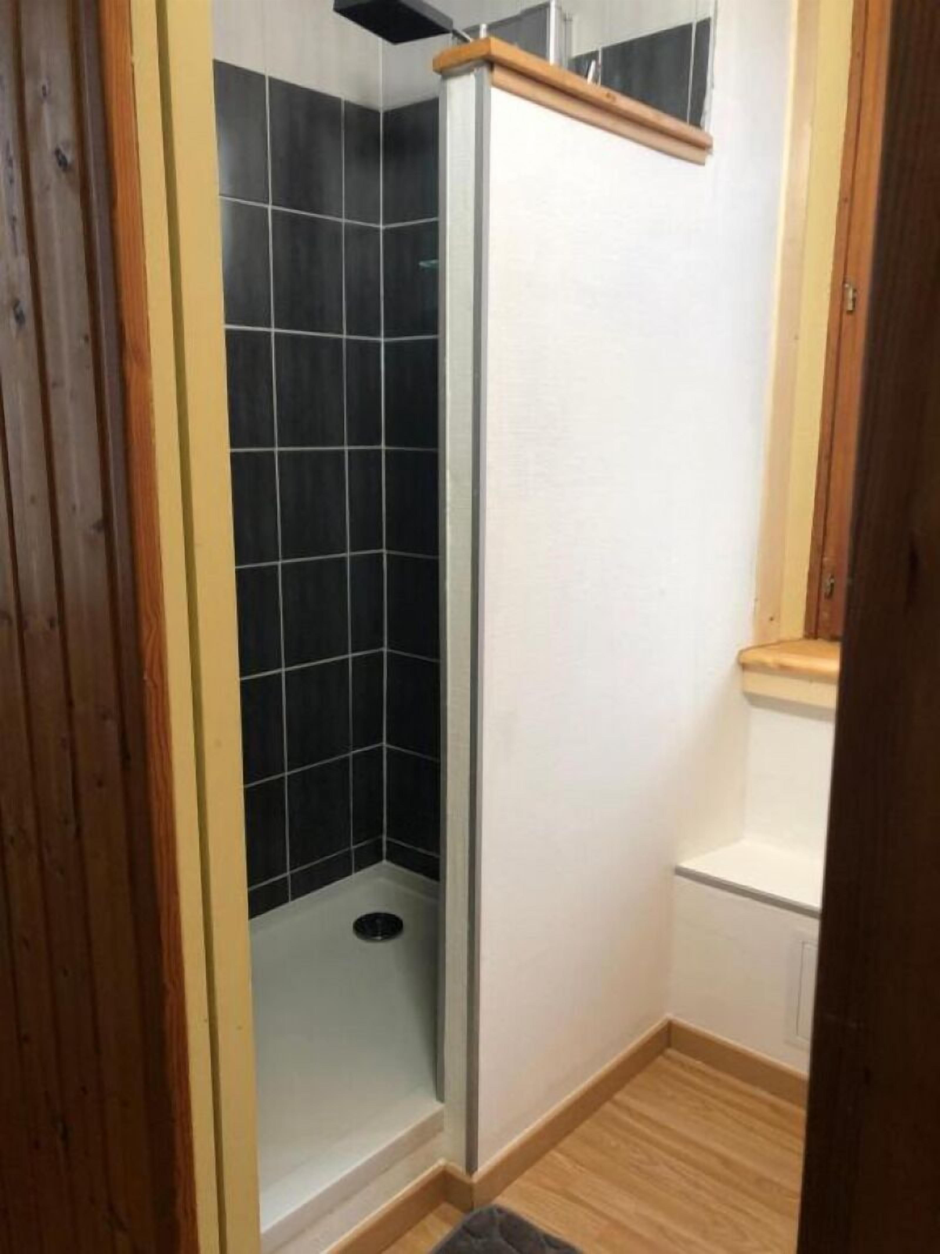 A small, enclosed shower area with black tiles and a wooden door frame.