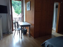 Quarto com piso de madeira, uma mesa, uma cadeira, uma lixeira pequena e uma cama.
