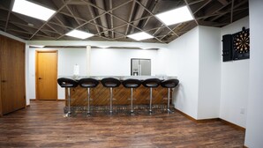A bar area with wooden flooring, a counter with stools, and a dartboard on the wall.