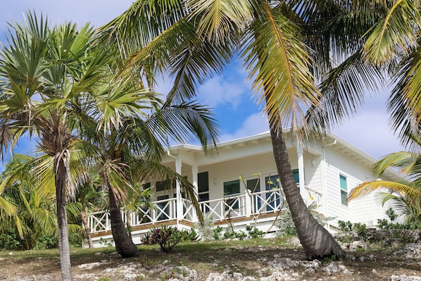 A white house with a balcony, surrounded by palm trees and a clear sky.
