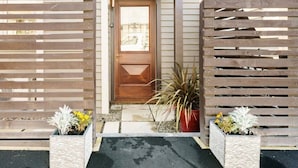 Uma porta de madeira com design geométrico, emoldurada por dois vasos com plantas e flores.