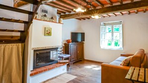 A cozy living room with a fireplace, wooden beams, a television, and a window with a view of greenery. - Stunning home in Stazzema with WiFi (Stazzema)