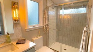 A modern bathroom with a glass shower enclosure, a toilet, and a vanity with a mirror. - Vashon View Cottage - Vashon, WA (Vashon)