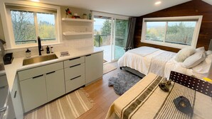 A modern bedroom with a large bed, a separate bathroom, and a kitchen area. - Vashon View Cottage - Vashon, WA (Vashon)