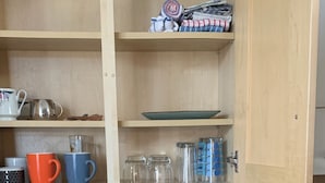A kitchen with wooden cabinets, a black countertop, a cutting board, a knife, a spray bottle, and a glass.