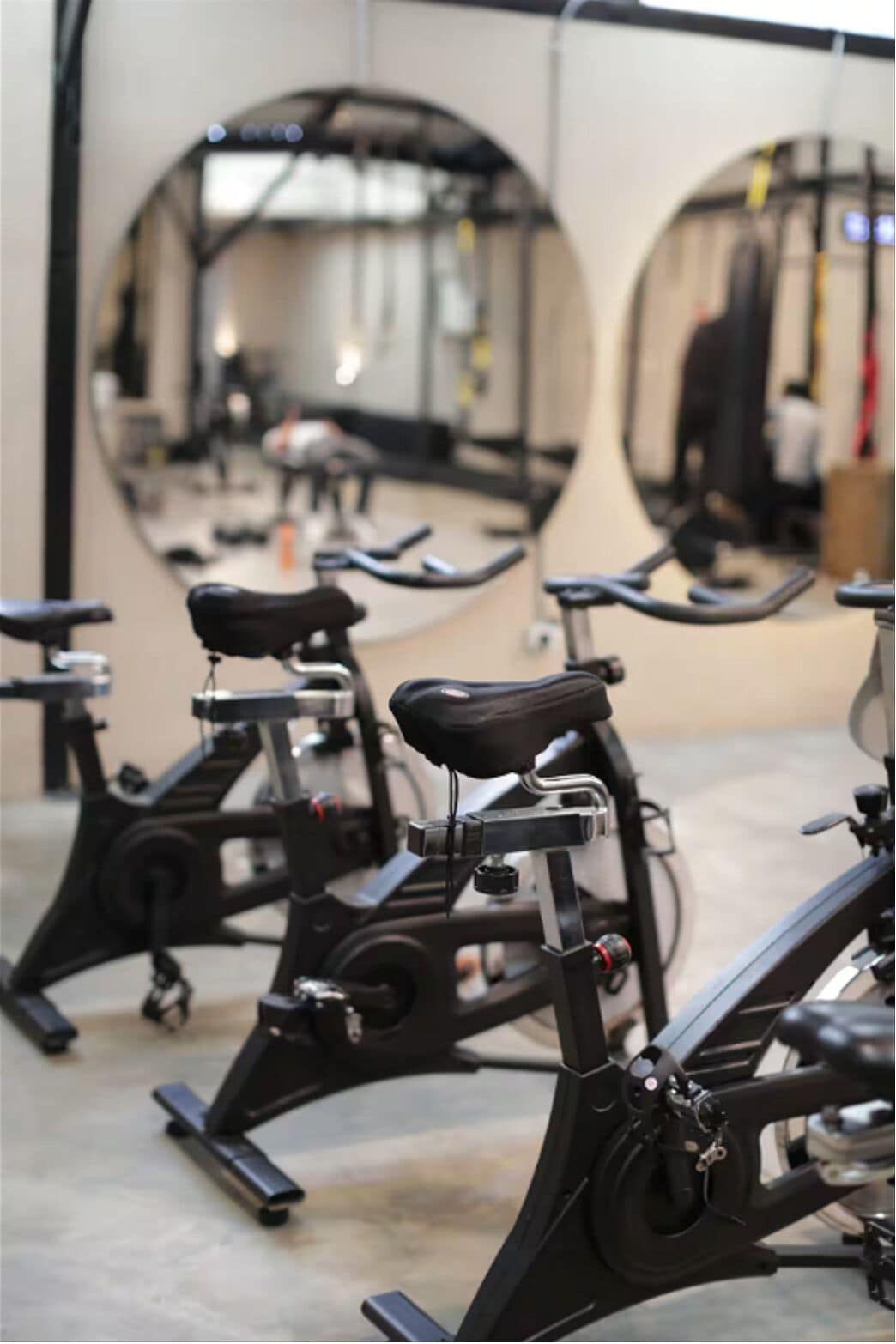 Un gimnasio con bicicletas estáticas dispuestas en filas, espejos grandes en las paredes y suelo de hormigón.