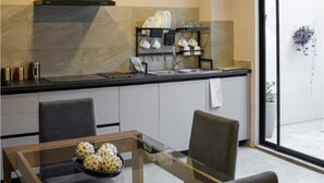 Una cocina moderna con extractor de aire negro, una mesa de comedor de cristal y vistas al exterior a través de un ventanal corredero.