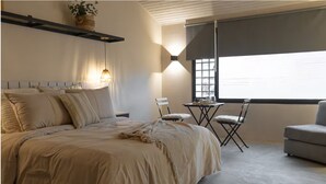 Un dormitorio con una cama grande, una pequeña mesa con sillas, un sofá y una ventana con persianas.