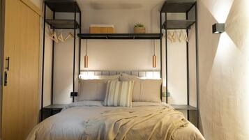 A bedroom with a bed, a shelf above the bed, and a wall-mounted light fixture.