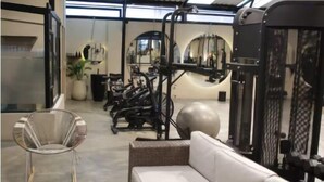 Un gimnasio con equipo de ejercicio, un sofá blanco y una silla de mimbre.