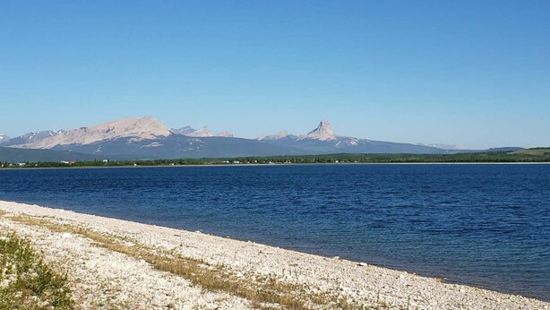 Eine Küstenlandschaft mit klarem Himmel, einem Kiesstrand und Bergen im Hintergrund.