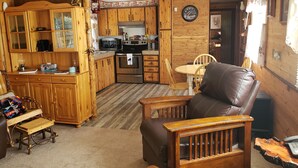 Ein gemütliches Interieur im Chalet-Stil mit Holzschränken, einer Küchenzeile, einem Essbereich mit Tisch und Stühlen sowie einem Ledersessel.