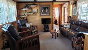 Ein gemütliches Blockhauss-Interieur mit Holzwänden, einem Ledersofa, einem Holztisch und einem Fernseher.