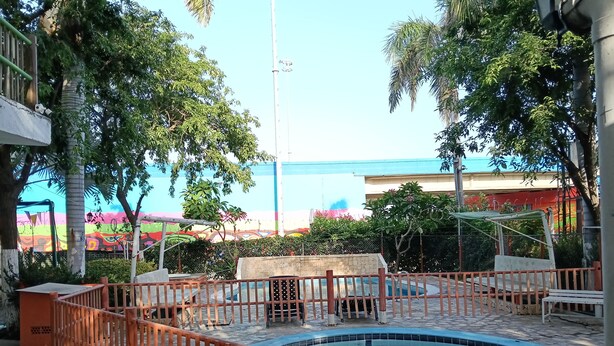 Zona de piscina con valla de madera, rodeada de árboles y un mural colorido de fondo.