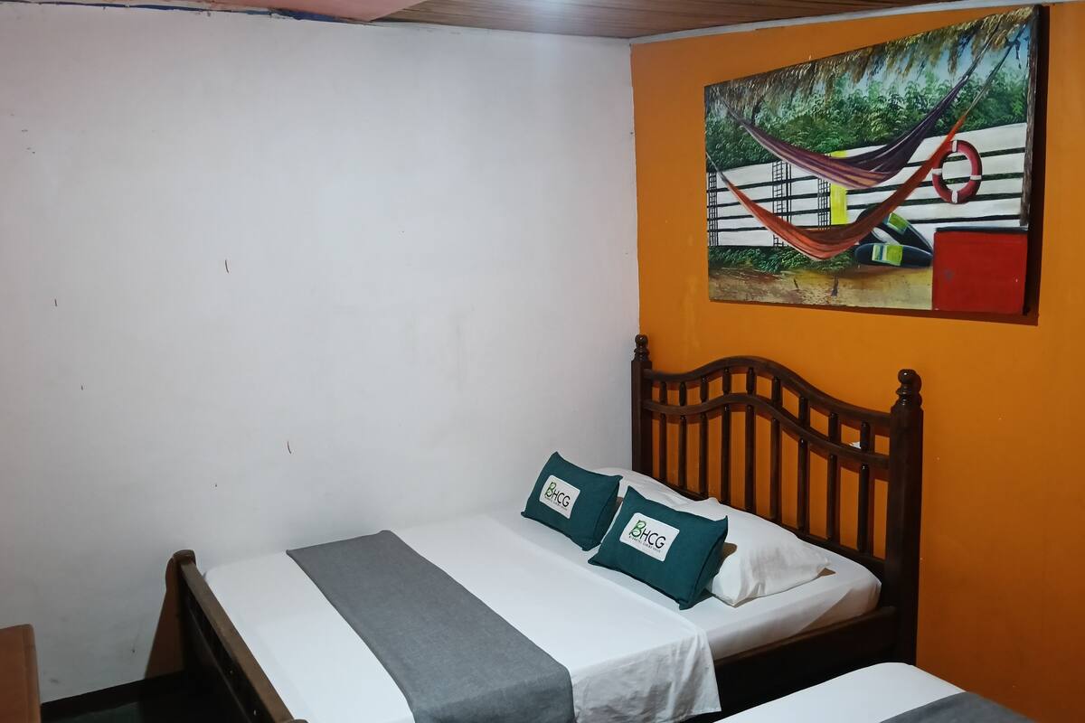 Una cama individual con cabecera de madera, una colcha gris y dos almohadas con un logotipo.