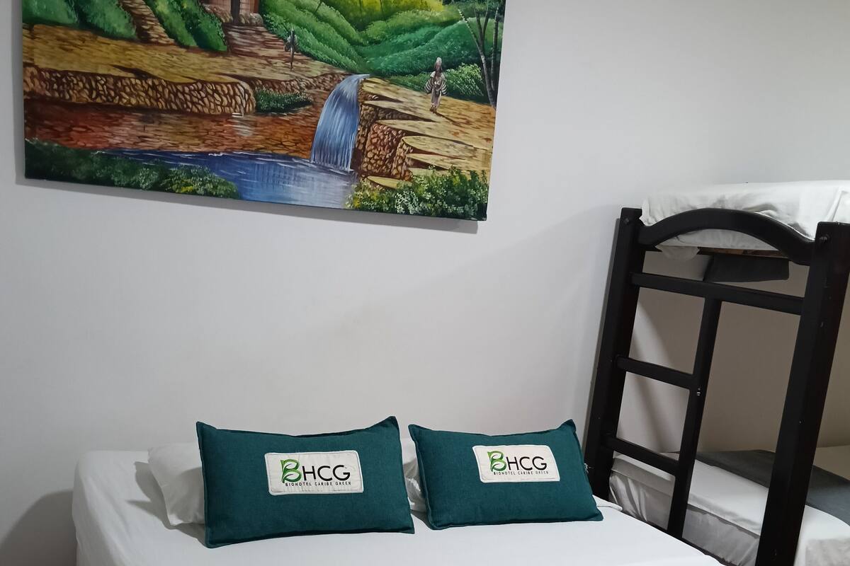 Una cama con dos almohadas etiquetadas "BHCG" y un cuadro de un paisaje rural sobre ella.