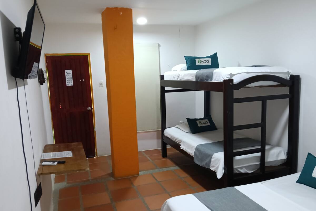 Habitación con literas, un televisor fijado a la pared, una puerta de madera y suelo de baldosas.