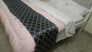 Una cama bien hecha con una colcha estampada y almohadas, un cabecero acolchado y un suelo de baldosas.
