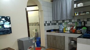 Cocina compacta con refrigerador, microondas y lavamanos. En primer plano, una mesa pequeña y un banco.