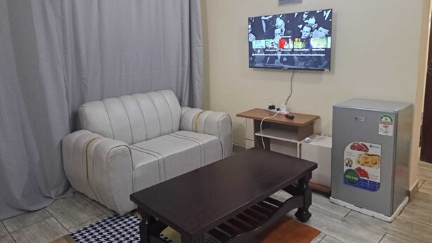 Una sala de estar con un sofá, una mesa de centro, un televisor montado en la pared y un refrigerador.