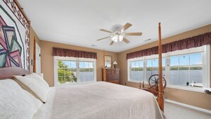 Ein Schlafzimmer mit einem großen Bett, einem Deckenventilator, einem Schminktisch und Fenstern mit Blick auf das Wasser.