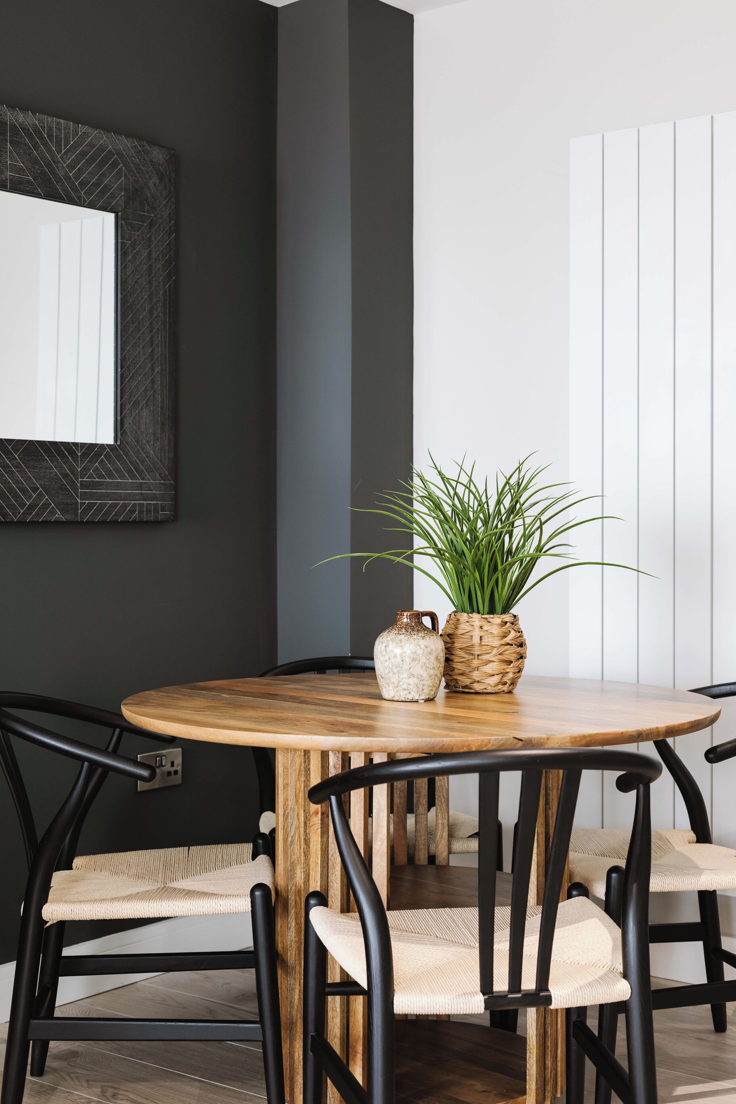 A dining area with a round wooden table, black chairs, and a potted plant.