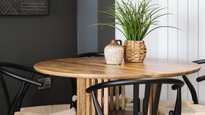 A dining area with a round wooden table, black chairs, and a potted plant.