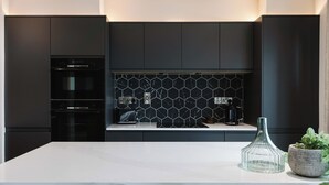 A modern kitchen with dark cabinetry, a marble countertop, and a hexagonal tile backsplash.