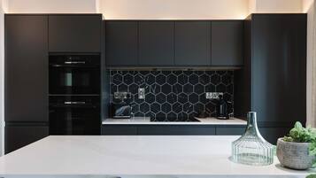 A modern kitchen with dark cabinetry, a marble countertop, and a hexagonal tile backsplash.